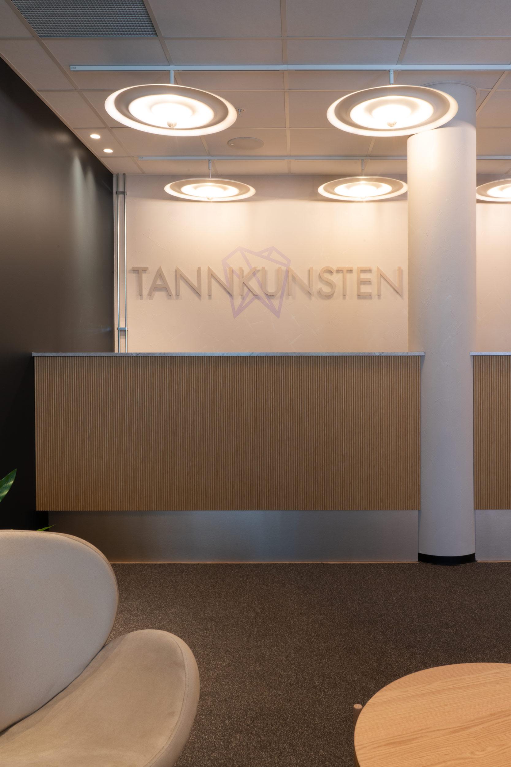 Resepsjonen i eikespiler, bakvegg med logo, og store runde lamper i taket